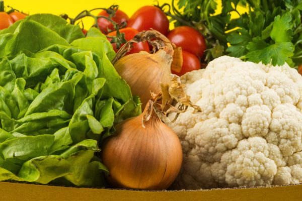 Fresh produce, food staples delivery or donation box concept on yellow background.